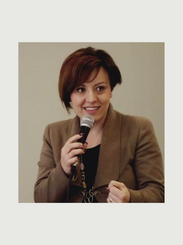 Woman in tan blazer speaking with a microphone